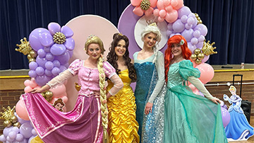 four princesses in colorful costumes posing in front of a balloon backdrop celebrating magical moments with nine characters from fairy tales